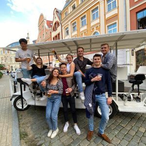 Friends posing with drinks around a beer bike in the colorful streets of Riga Old Town