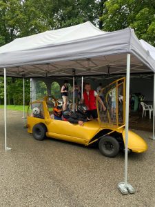 Participants getting into a yellow summer bobsleigh under a tent in Latvia