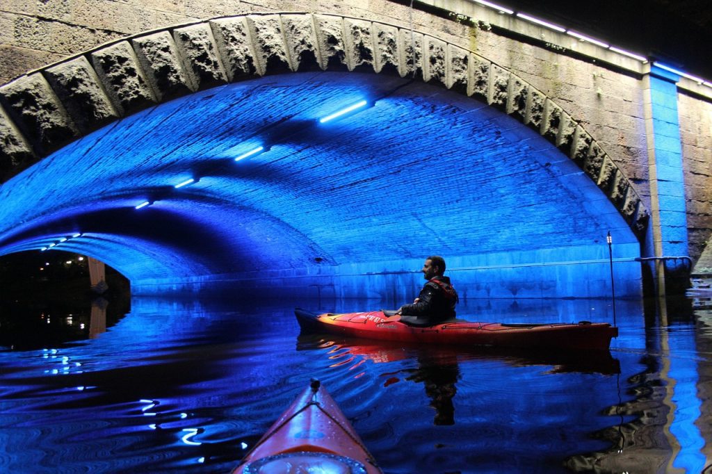 Man kayaking under an illuminated bridge in Riga at night