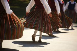 Latvian women performing a traditional folk dance in colorful striped skirts.