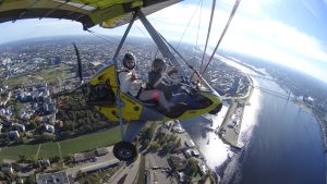 Two people flying a yellow ultralight trike over Riga city and Daugava river