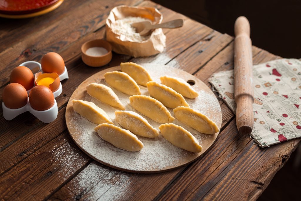Handmade dumplings arranged on a floured wooden board with baking ingredients on a rustic table.