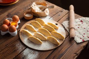 Handmade dumplings arranged on a floured wooden board with baking ingredients on a rustic table.
