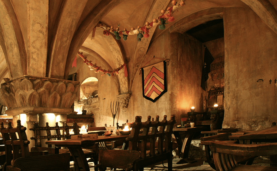 Medieval-style dining room with wooden chairs, banners, and warm lighting