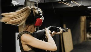 Woman with ponytail aiming a shotgun at an indoor range