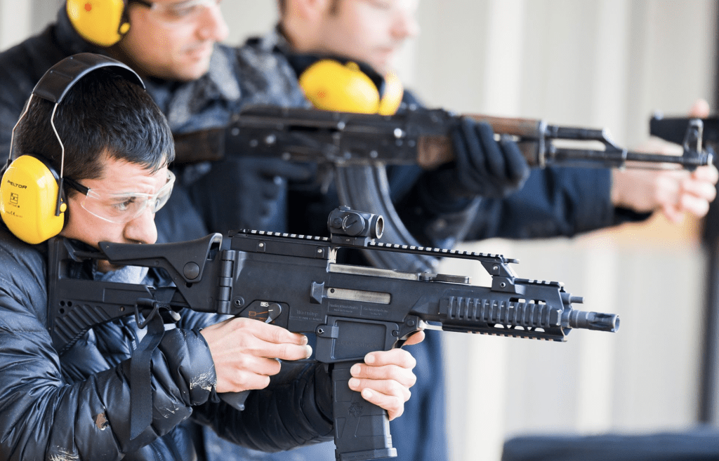 Man aiming a tactical rifle at outdoor shooting range with instructor