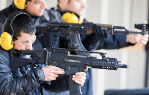 Man aiming a tactical rifle at outdoor shooting range with instructor