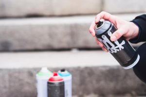 Close-up of a hand holding a black spray paint can with colorful cans in the background