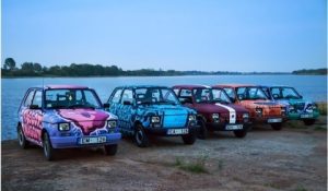Decorated rally cars parked by a lake during Pan Car Rally in Latvia