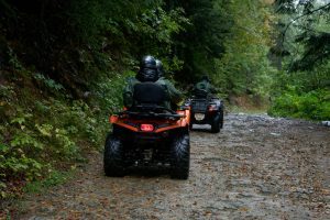Two riders on quad bikes driving through a wet forest trail