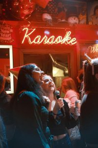 Women singing together at a karaoke party under neon lights