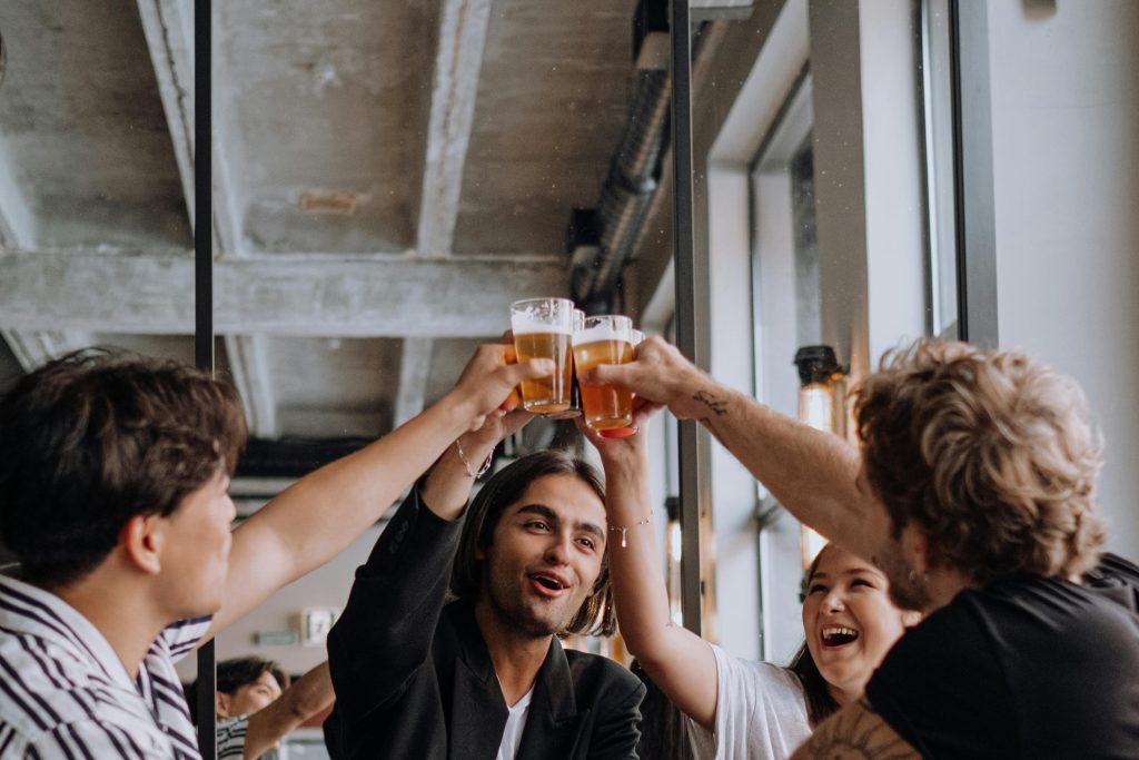 Friends cheering with pints of beer at a modern bar.