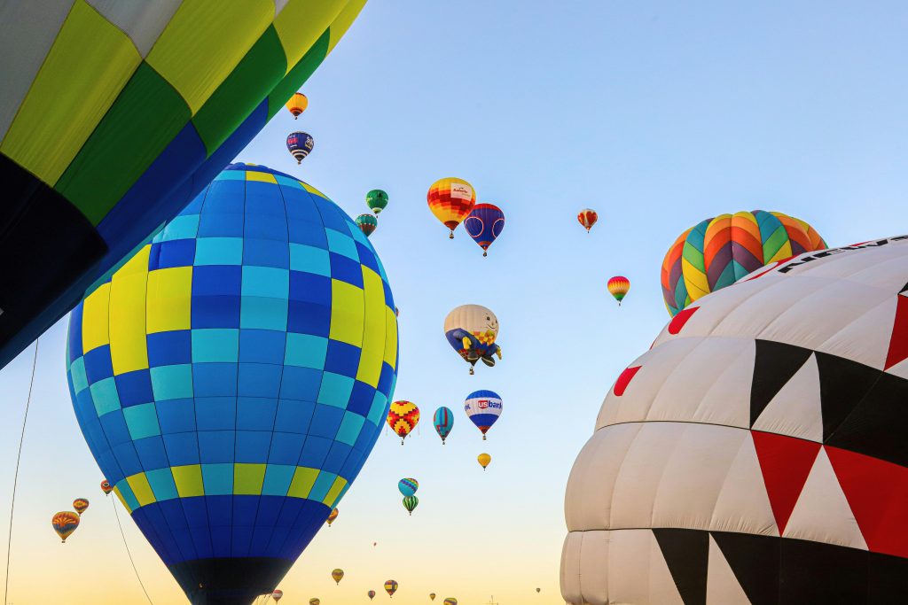 Aerial view of a colorful hot air balloon floating over green fields and forests