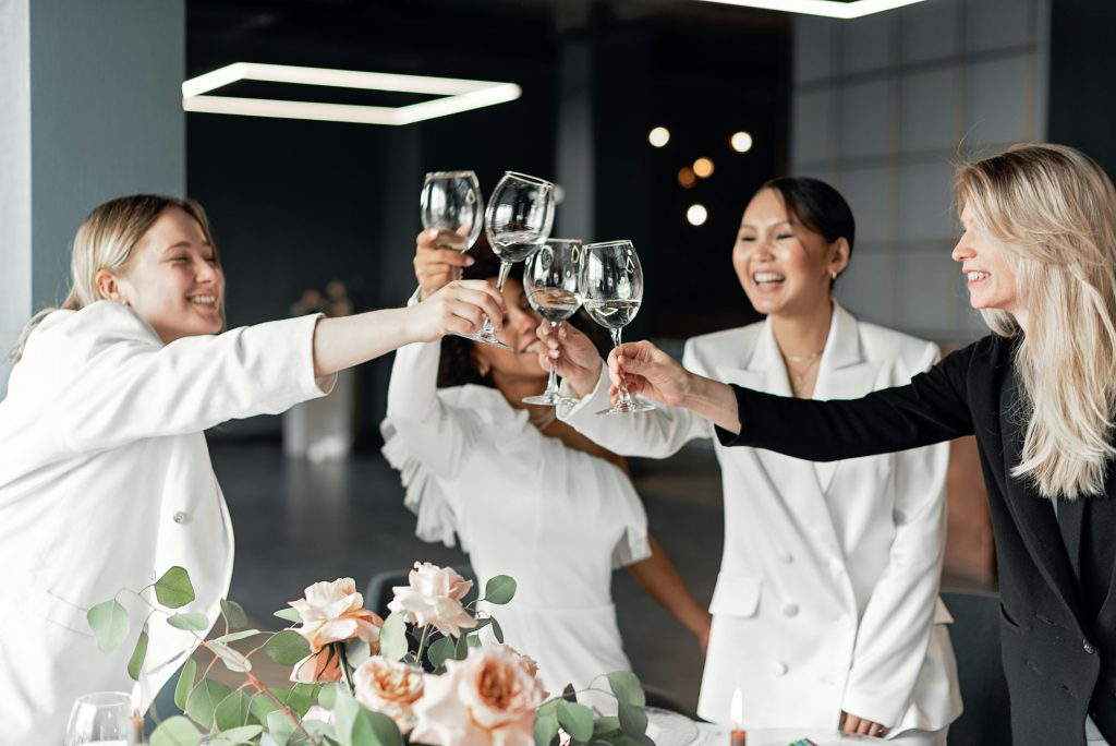 Group of women in white suits raising glasses in celebration.