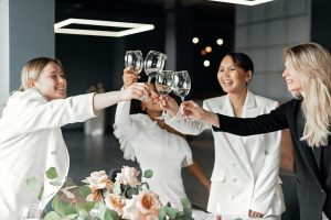 Group of women in white suits raising glasses in celebration.