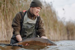 Man holding a large carp while standing in shallow water