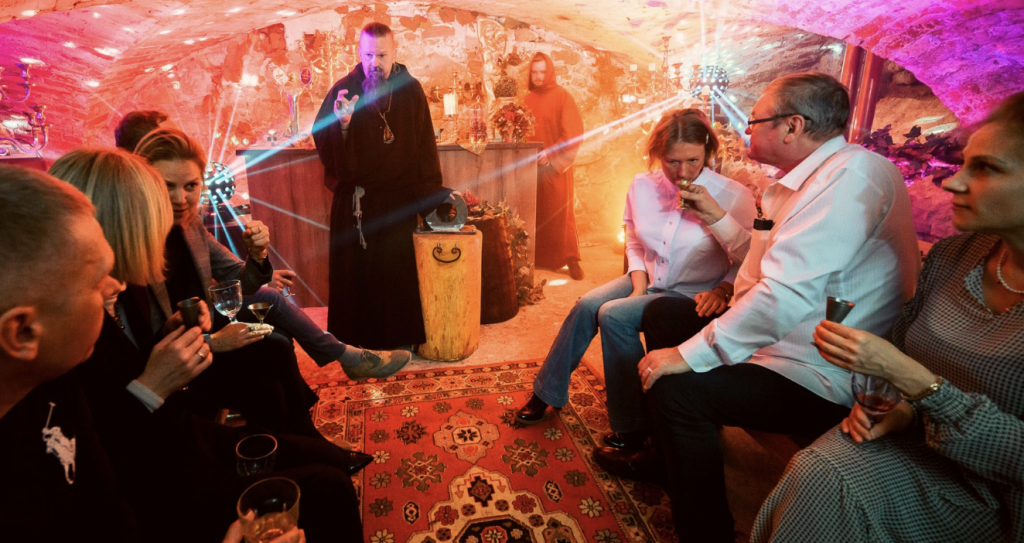 Guests sitting in a medieval cellar while a monk leads a degustation ceremony